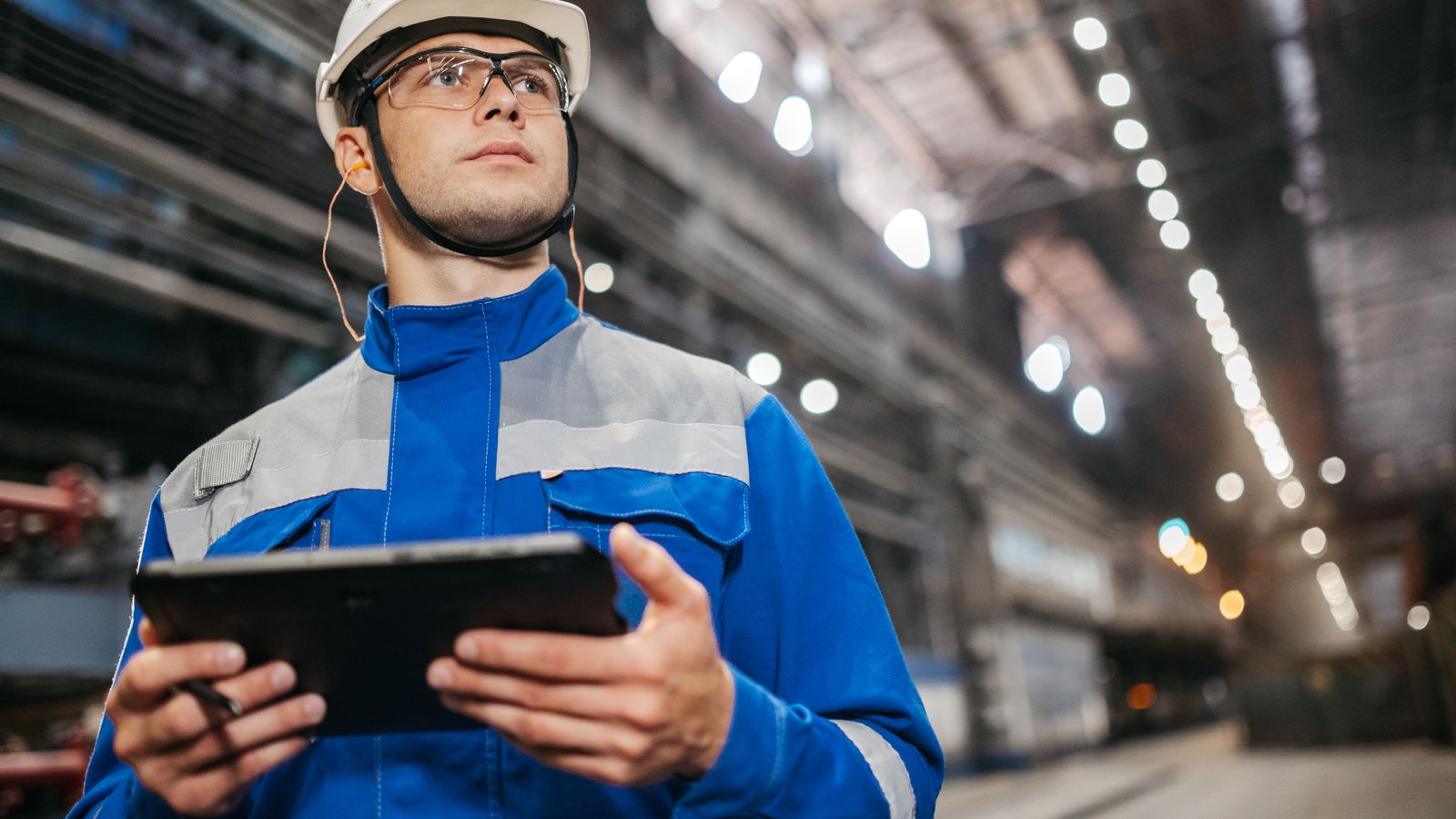 Industrial technician in a hard hat using a tablet on the plant floor